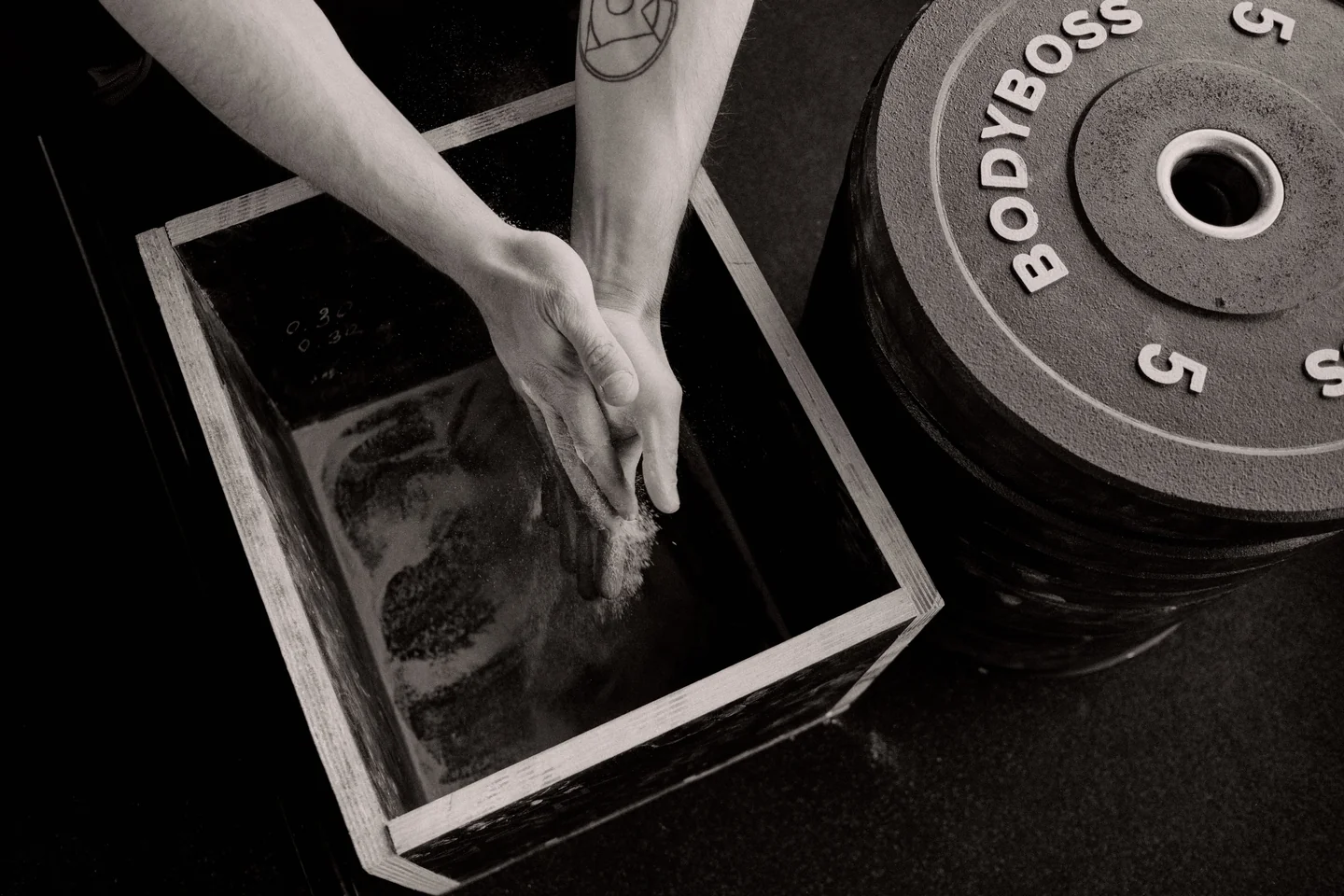 A lifter chalking their hands next to a loaded barbell plate before a heavy set