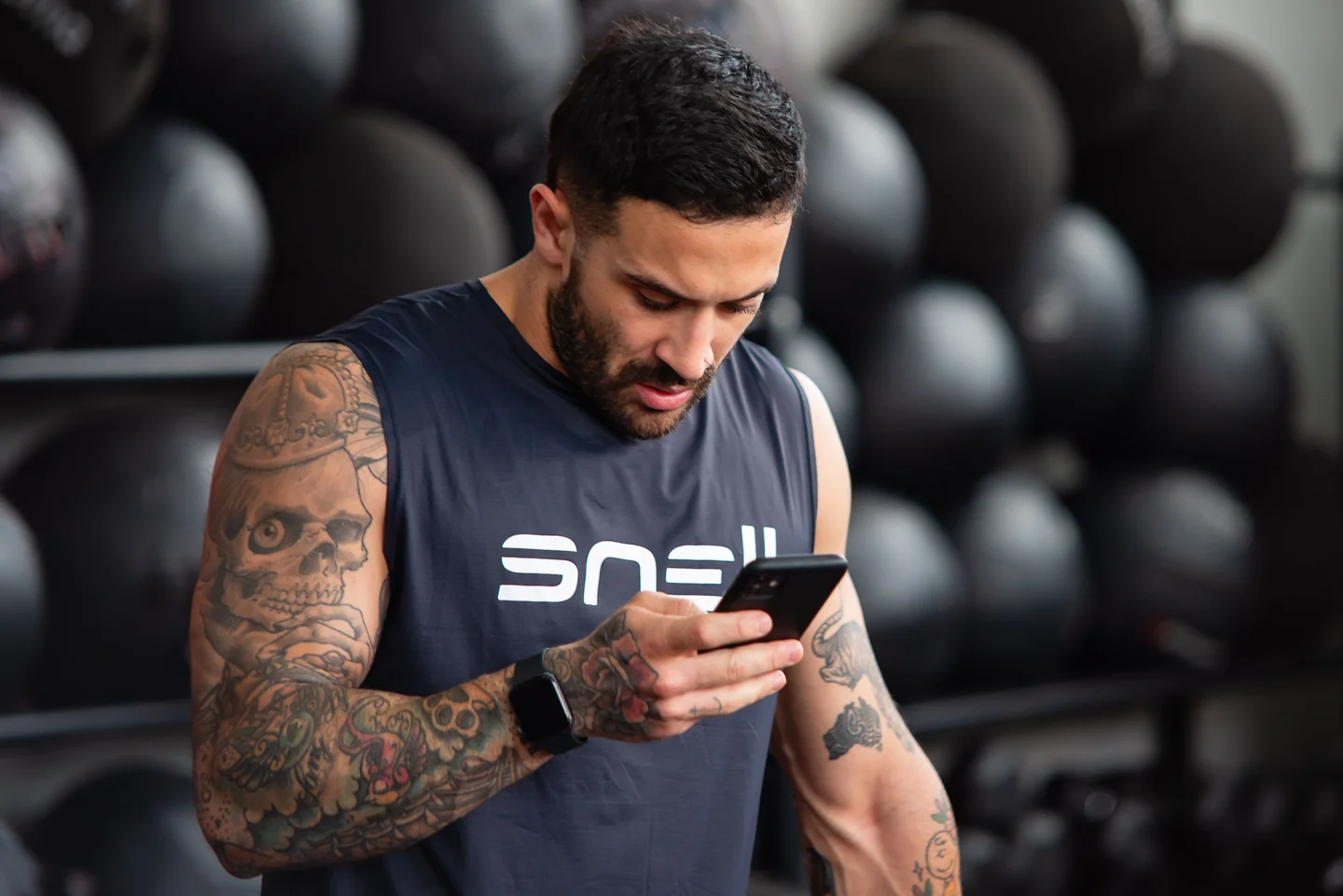 A lifter checking his phone between sets in front of a dumbbell rack