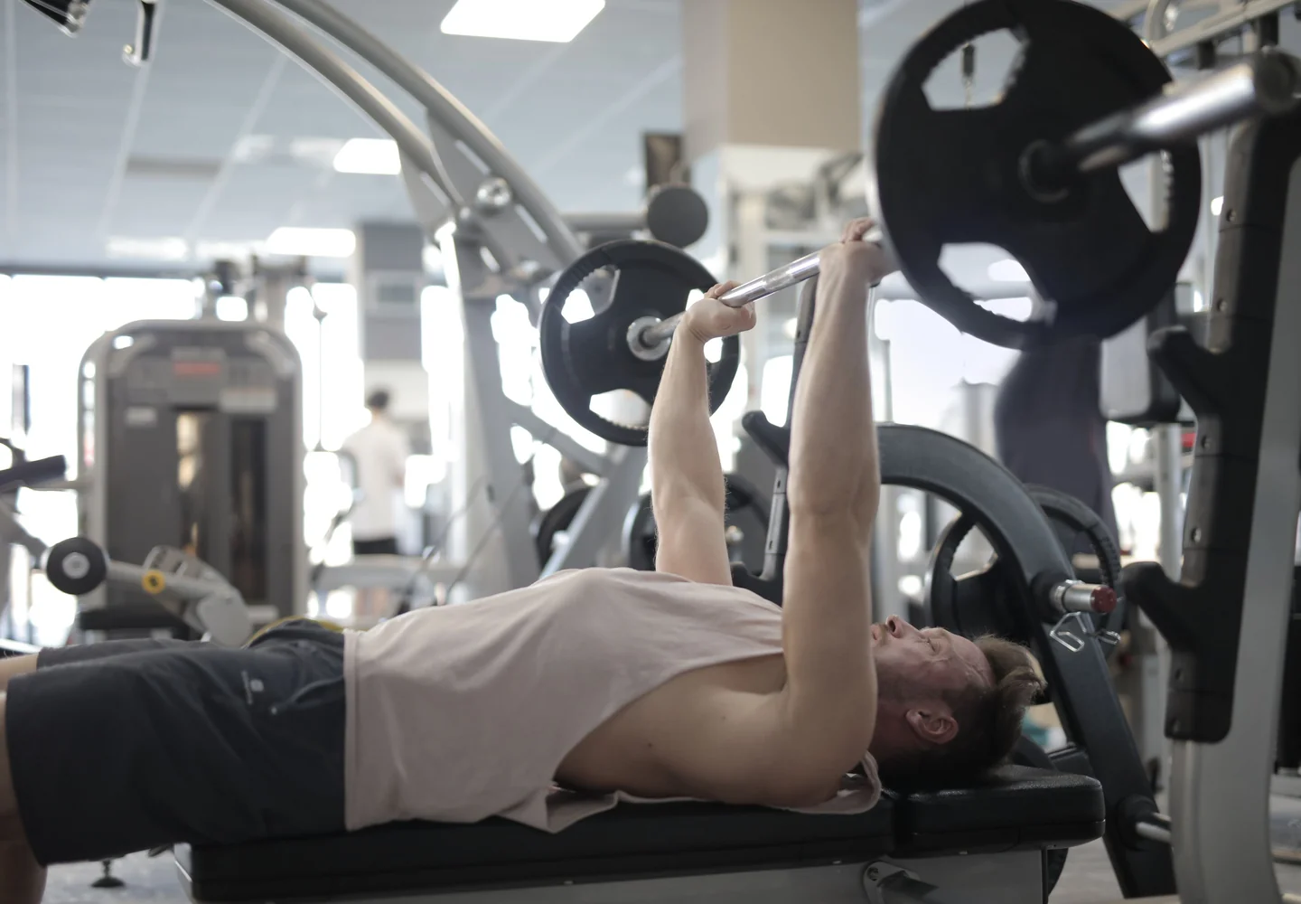 Un levantador haciendo press de banca en un gimnasio comercial lleno de máquinas