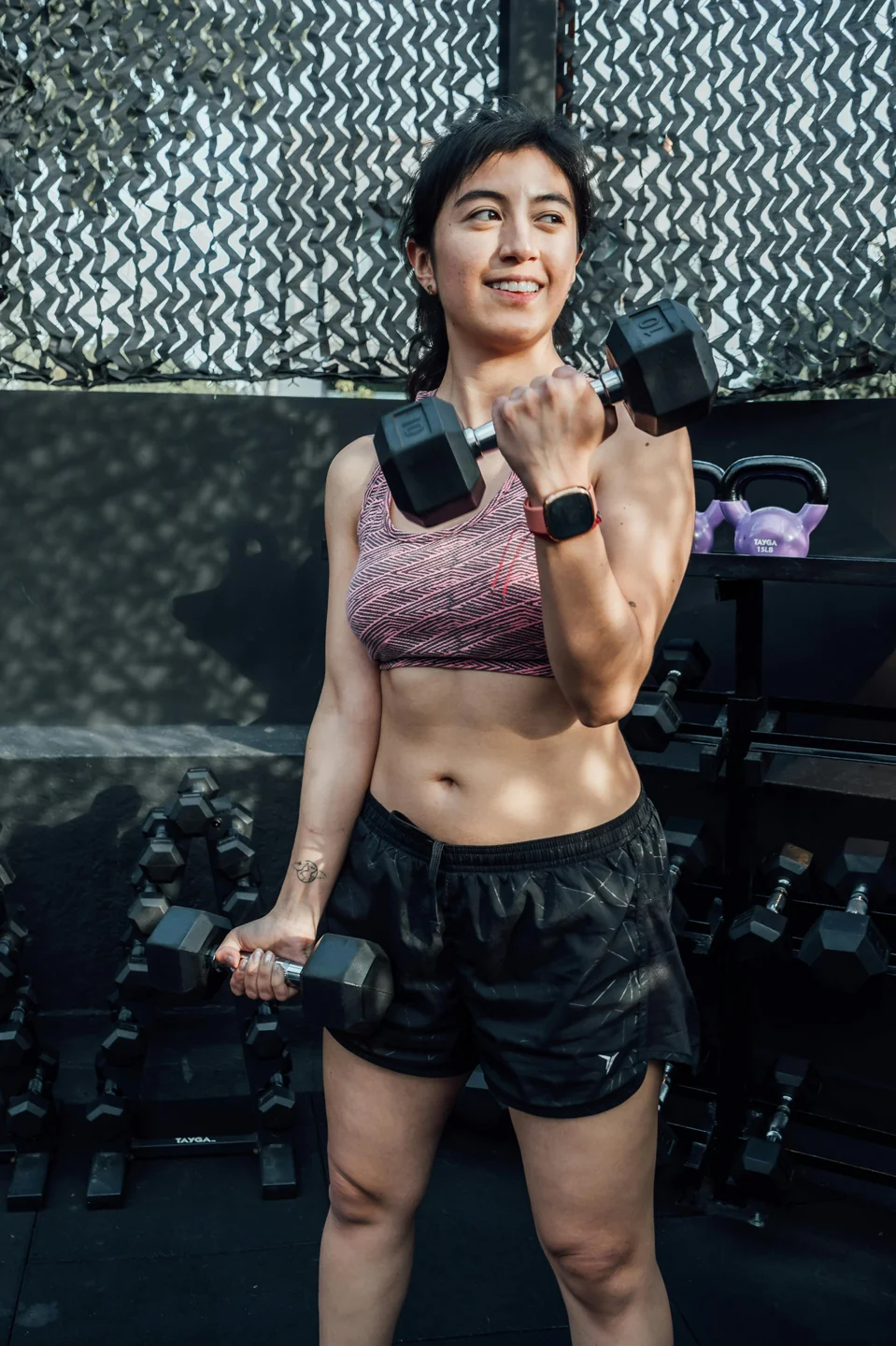 A woman doing a dumbbell curl in a home gym, smiling